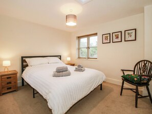 A bedroom with a bed, bedside tables, a chair, a window with blinds, and wall-mounted pictures. - Stone Cottage (Church Stretton)
