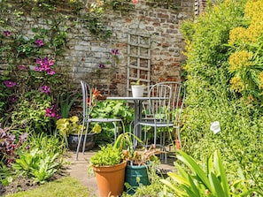 Ein Garten mit Backsteinmauer, Metallstühlen und Topfpflanzen.
