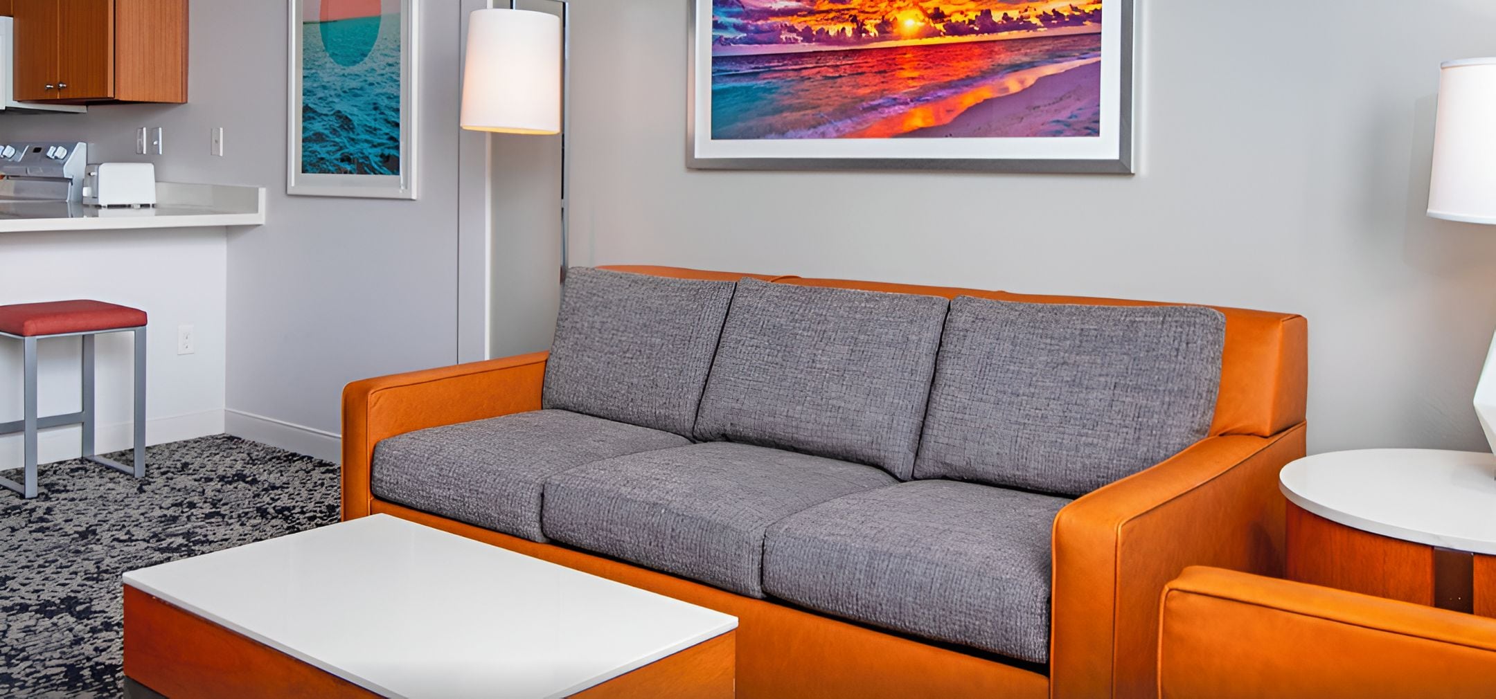 A modern living room with a grey sofa, a white coffee table, and a kitchen area with a toaster.