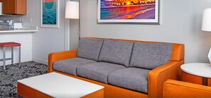 Ett modernt vardagsrum med en grå soffa, ett vitt soffbord och en köksdel med en brödrost.