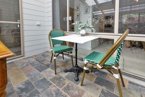 A patio area with a table and two chairs, a potted plant, and a view through a glass door. - Kingfisher:  All about relaxed Raymond Island living (Raymond Island)