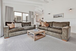 A modern living room with two grey sofas, a wooden coffee table, and a large window with curtains. - Kingfisher:  All about relaxed Raymond Island living (Raymond Island)