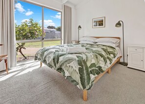 Une chambre à coucher avec un grand lit, une fenêtre avec des rideaux, une lampe de chevet et une petite armoire.