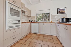 A kitchen with white cabinets, a built-in oven, a dishwasher, and a microwave. - Kingfisher:  All about relaxed Raymond Island living (Raymond Island)