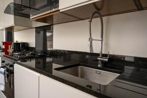 A modern kitchen with a stainless steel sink, black countertop, and a gas stove. - Berwick Soho Suites by Aureva Residences (London)