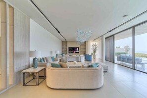 Ein modernes Wohnzimmer mit einer großen Couch, einem Couchtisch und einem Fernseher. Ein großes Fenster bietet einen Blick ins Freie.