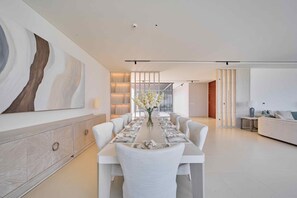 A modern dining area with a long table set for six, a large abstract painting on the wall, and a minimalist interior design. - Sleek 4BR Villa | Private Pool & Beach | Al Zorah (Ajman)