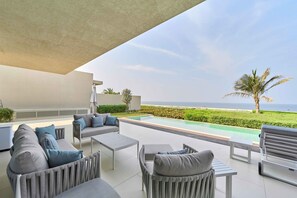 A modern outdoor seating area with a pool, overlooking a beach and ocean. - Sleek 4BR Villa | Private Pool & Beach | Al Zorah (Ajman)