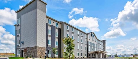 A multi-story hotel with a modern design, featuring a central entrance and a parking area.