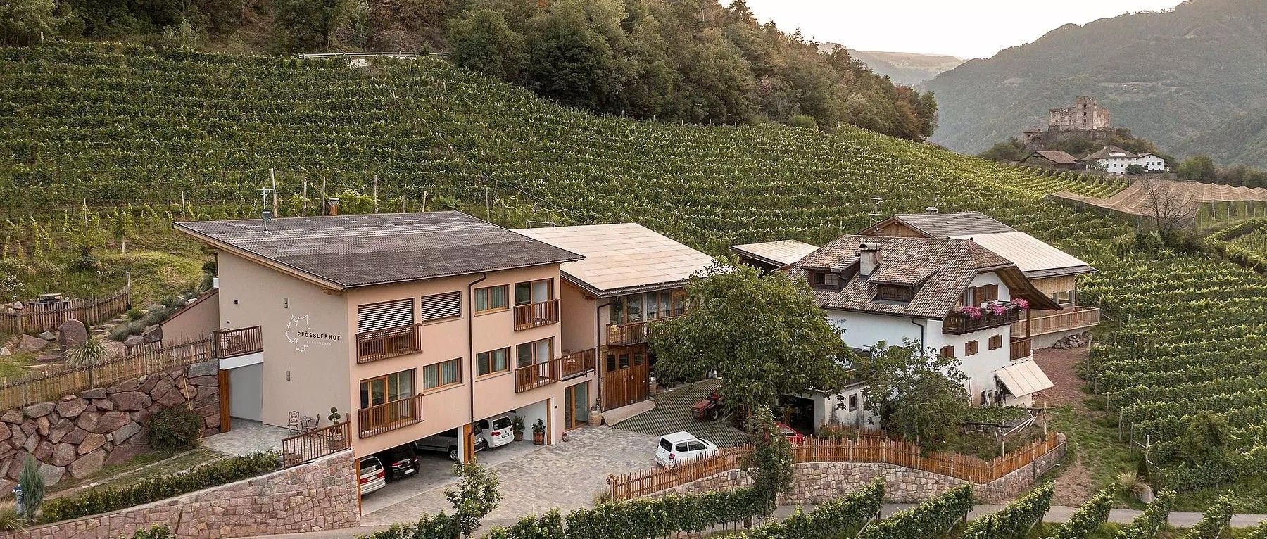 Un immeuble à plusieurs étages doté de balcons, d’un mur en pierre et, au fond, d’un vignoble.