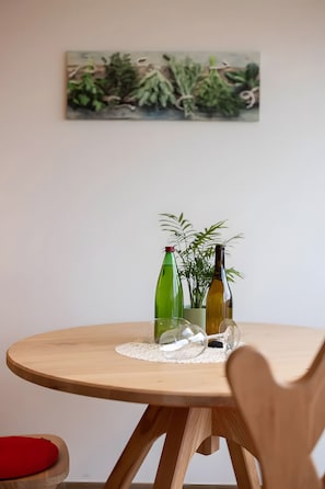 A round wooden table with two bottles and a glass, a potted plant, and a painting on the wall. - Apartment 'Pfösslerhof Fichte' with Mountain View, Shared Pool and Wi-Fi (Bolzano)