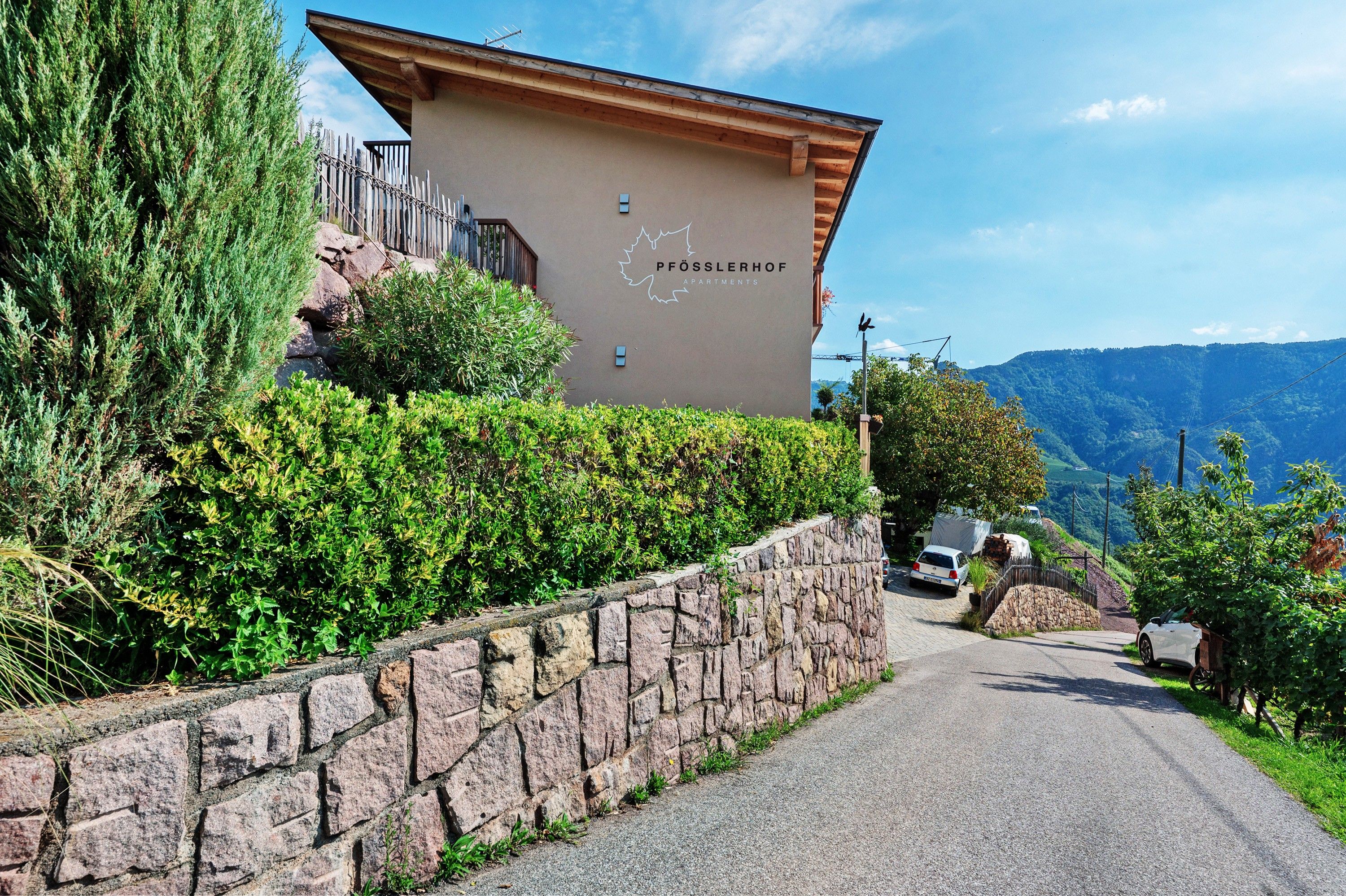 A building with a stone wall and a wooden fence, labeled 'PFÖSSLERHOF FARMS,' with a road leading to it.