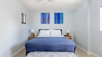 A bedroom with a bed, two nightstands, a ceiling fan, and two wall-mounted paintings.