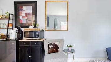 A compact living space with a kitchenette, a sofa, a small round table with a plant, and a large mirror.