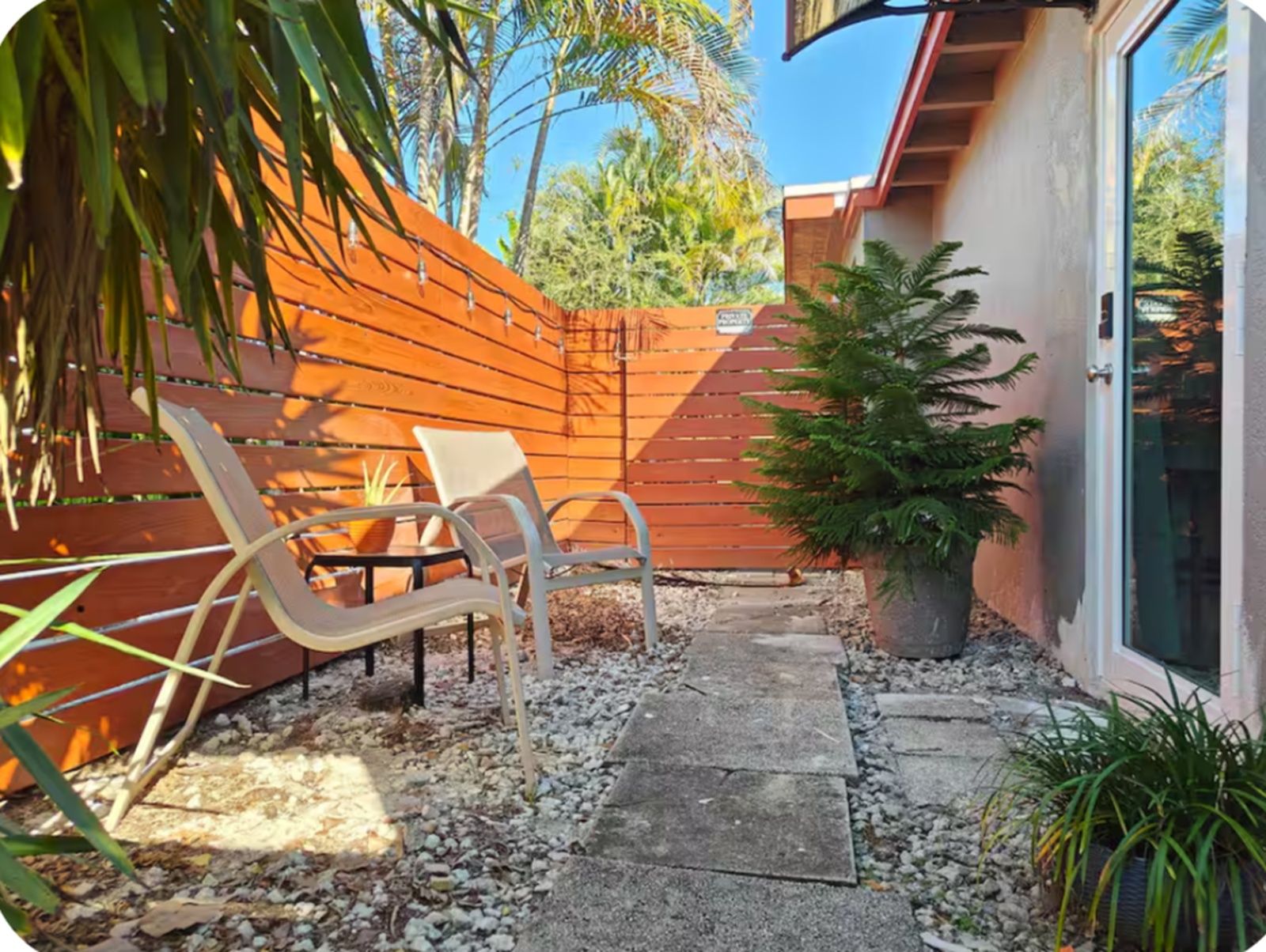 A patio area with a wooden fence, a concrete pathway, and a potted plant.