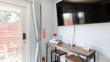 A room with a television mounted on the wall, a small table with stools, and a fire extinguisher on the wall.