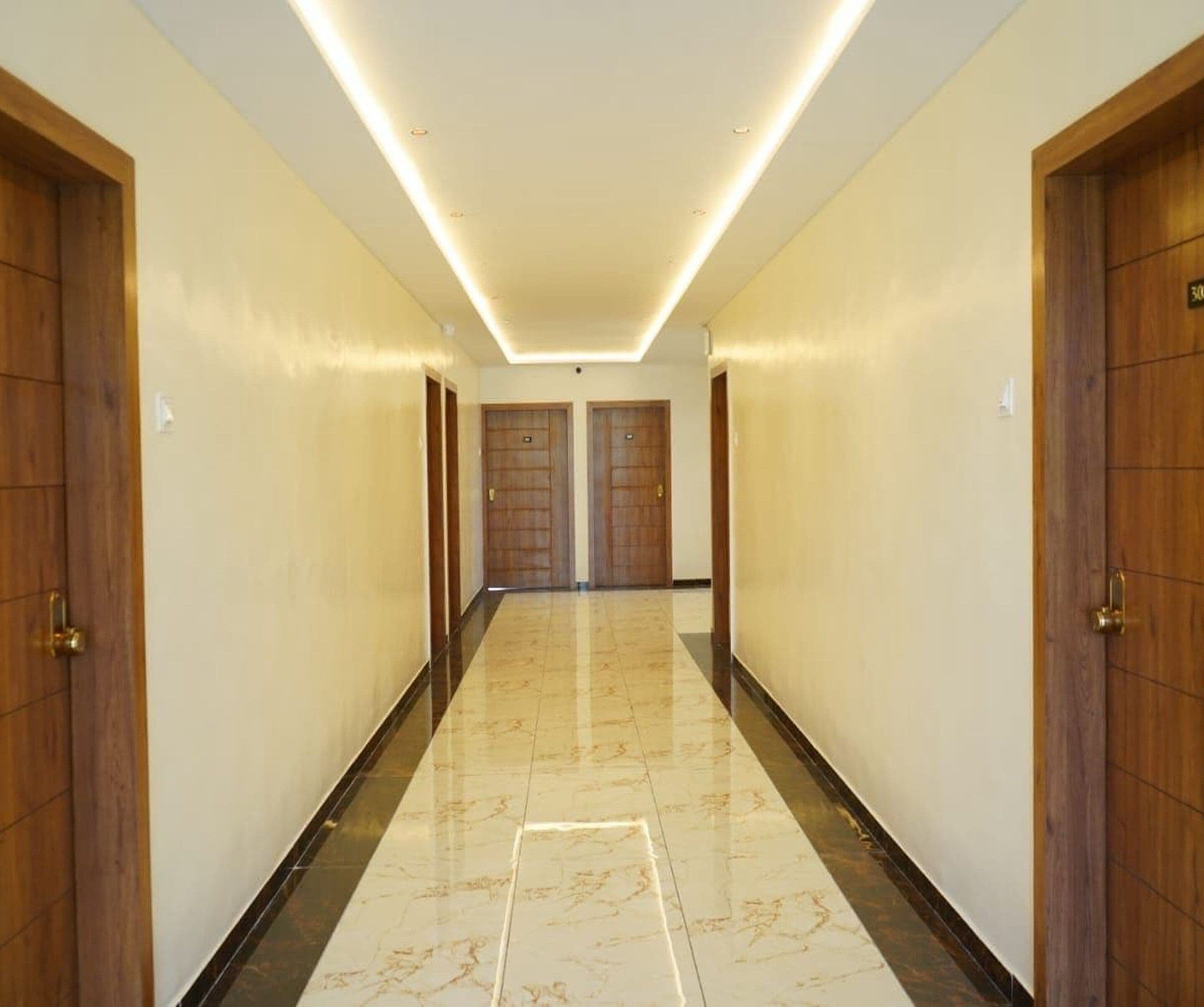 A corridor with two wooden doors, a tiled floor, and a ceiling with recessed lighting.