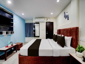 A modern hotel room with a large bed, a bedside table, a small table with a plant, and an air conditioning unit. - Classic Hotel Khushi IN (Bhubaneshwar)