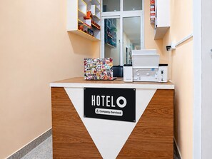 A hotel reception desk with a 'HOTEL O' sign, a company-serviced label, and a colorful bag on top. - Classic Hotel Khushi IN (Bhubaneshwar)