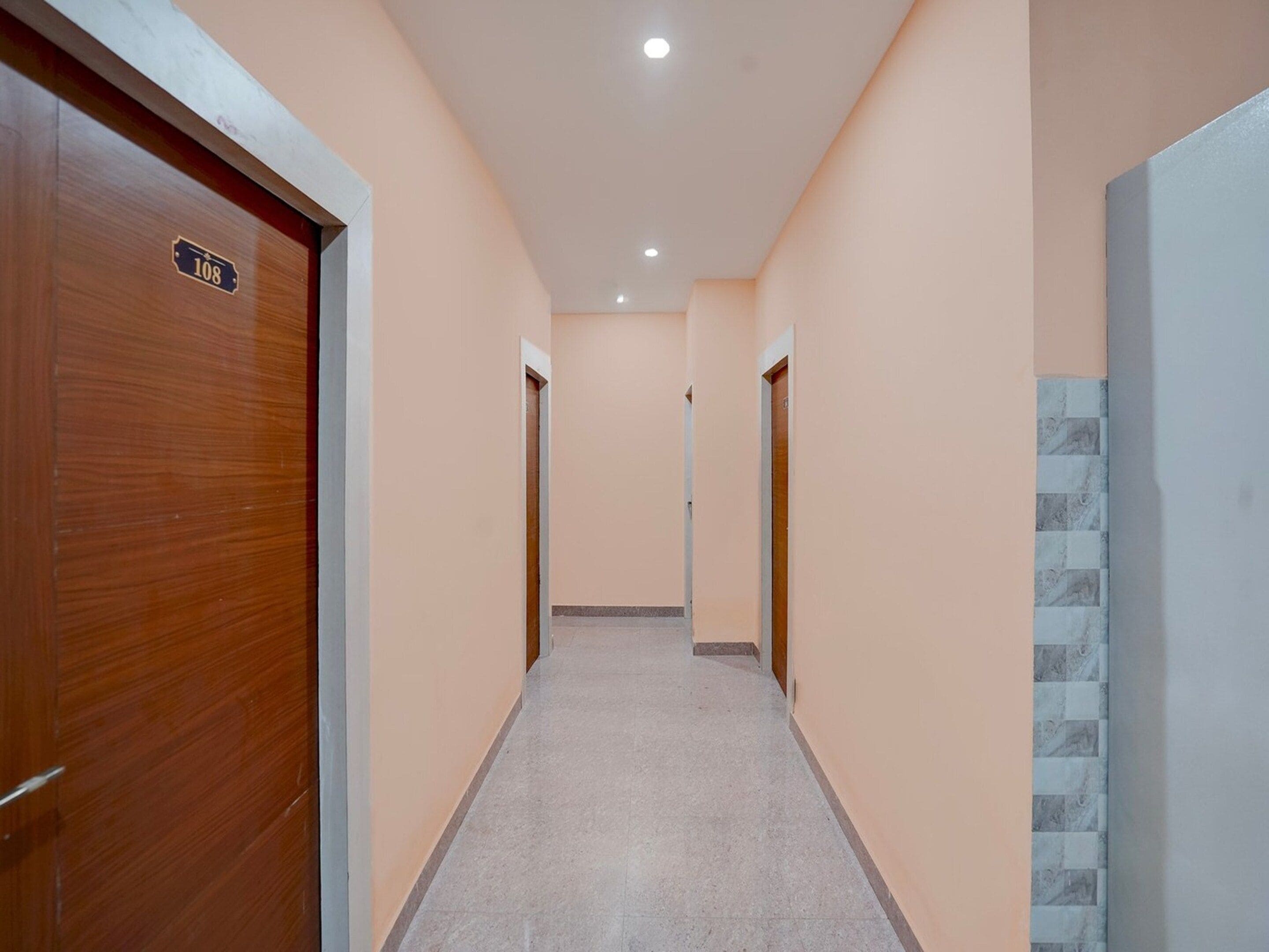 A hallway with a wooden door on the left, a tiled wall on the right, and a tiled floor.
