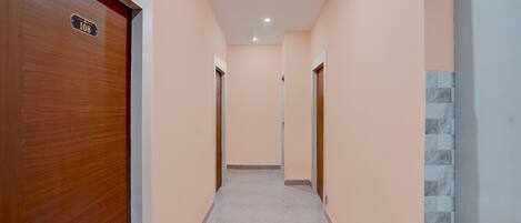 A hallway with a wooden door on the left, a tiled wall on the right, and a tiled floor.