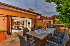 An outdoor dining area with a checkered tablecloth, surrounded by chairs, and a view of the house interior. - Luxurious 4-bedroom Villa With Private Pool in Hartbeespoort (Hartbeespoort)