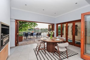 A dining area with a round table, chairs, and a view of a lake. - Luxurious 4-bedroom Villa With Private Pool in Hartbeespoort (Hartbeespoort)