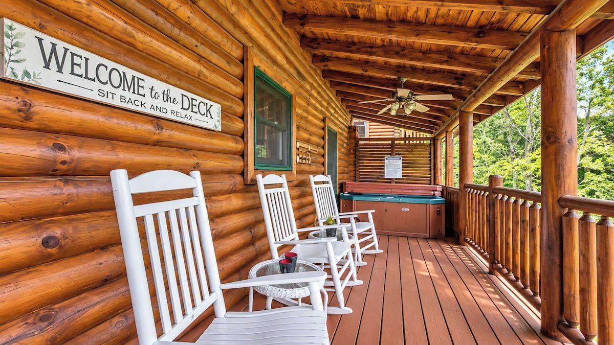Eine Holzterrasse mit einem Willkommensschild, Sitzgelegenheiten im Freien und Blick auf den umliegenden Wald.