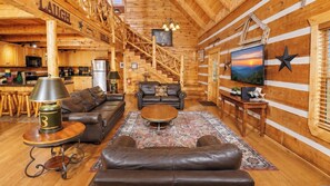 A log cabin interior with a living room, kitchen, and a staircase. - Beautiful Log Cabin 3BR, Loft, Games, Hot Tub (Sevierville)