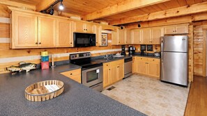 A wooden-paneled kitchen with stainless steel appliances, a coffee maker, and a fish decoration. - Beautiful Log Cabin 3BR, Loft, Games, Hot Tub (Sevierville)
