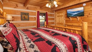 A log cabin room with a bed, a television, and a window with curtains. - Beautiful Log Cabin 3BR, Loft, Games, Hot Tub (Sevierville)
