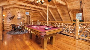 Een houten interieur met een pooltafel, stoelen en een plafond met houten balken.