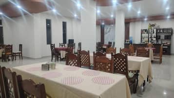 A dining area with multiple tables and chairs, a kitchen area in the background, and a ceiling with recessed lighting.