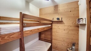 Ein Etagenbett mit Holz-Kopfteil, ein Regal mit einem kleinen dekorativen Gegenstand und ein Wandregal mit einem Buch und einer kleinen Pflanze.