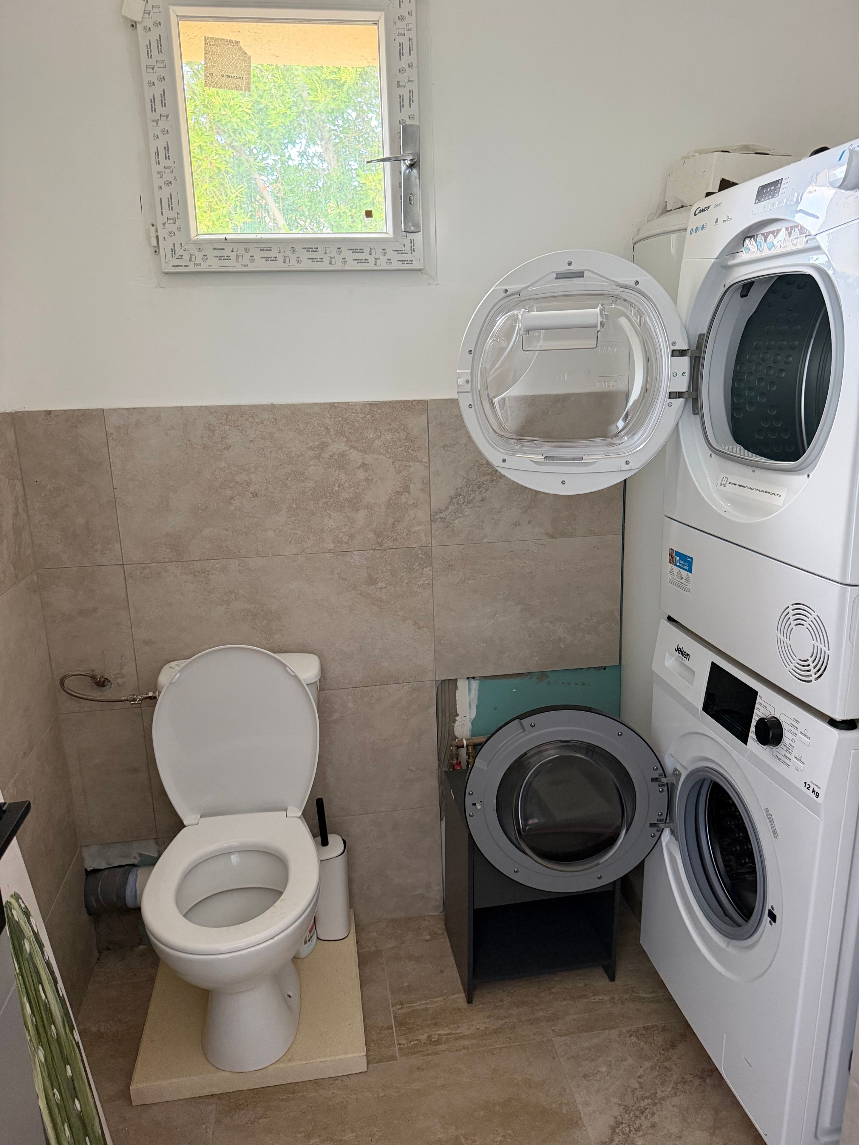 Ein kleines Badezimmer mit Toilette, Waschmaschine und kleinem Fenster.