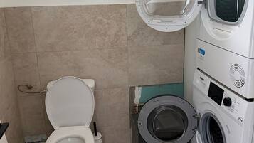 Ein kleines Badezimmer mit Toilette, Waschmaschine und kleinem Fenster.