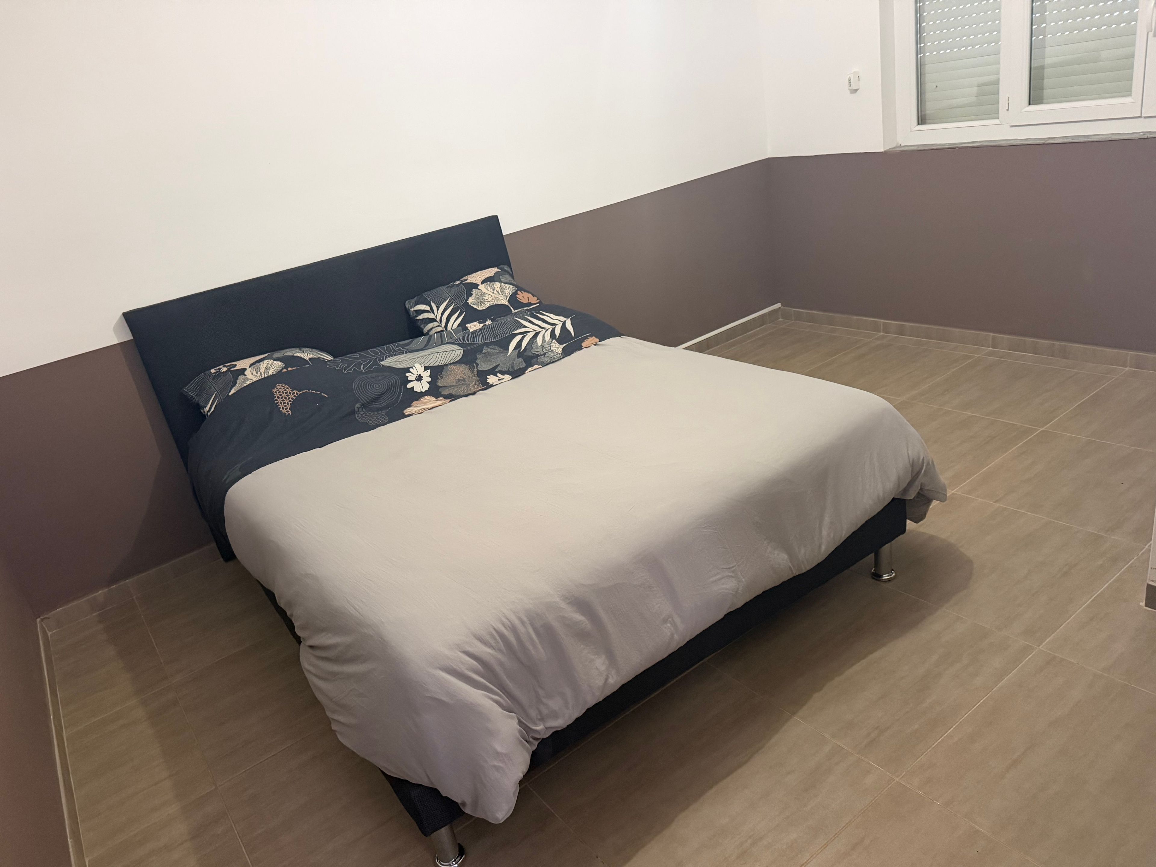 Een enkel bed met een donker hoofdbord en een witte matras in een kamer met een bruine vloer en een bruine wand.