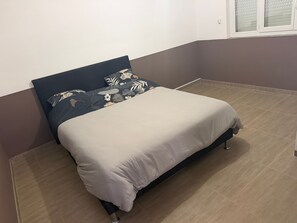 A single bed with a dark headboard and a white mattress in a room with a brown floor and a brown wall.