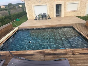 A swimming pool with a wooden deck and a stone wall.
