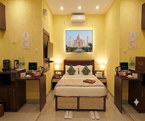 A hotel room with a bed, nightstands, a flat-screen TV, a wall-mounted air conditioner, and a framed picture of the Taj Mahal. - Deluxe Room Jessore Road Kolkata Airport (Barakpur)