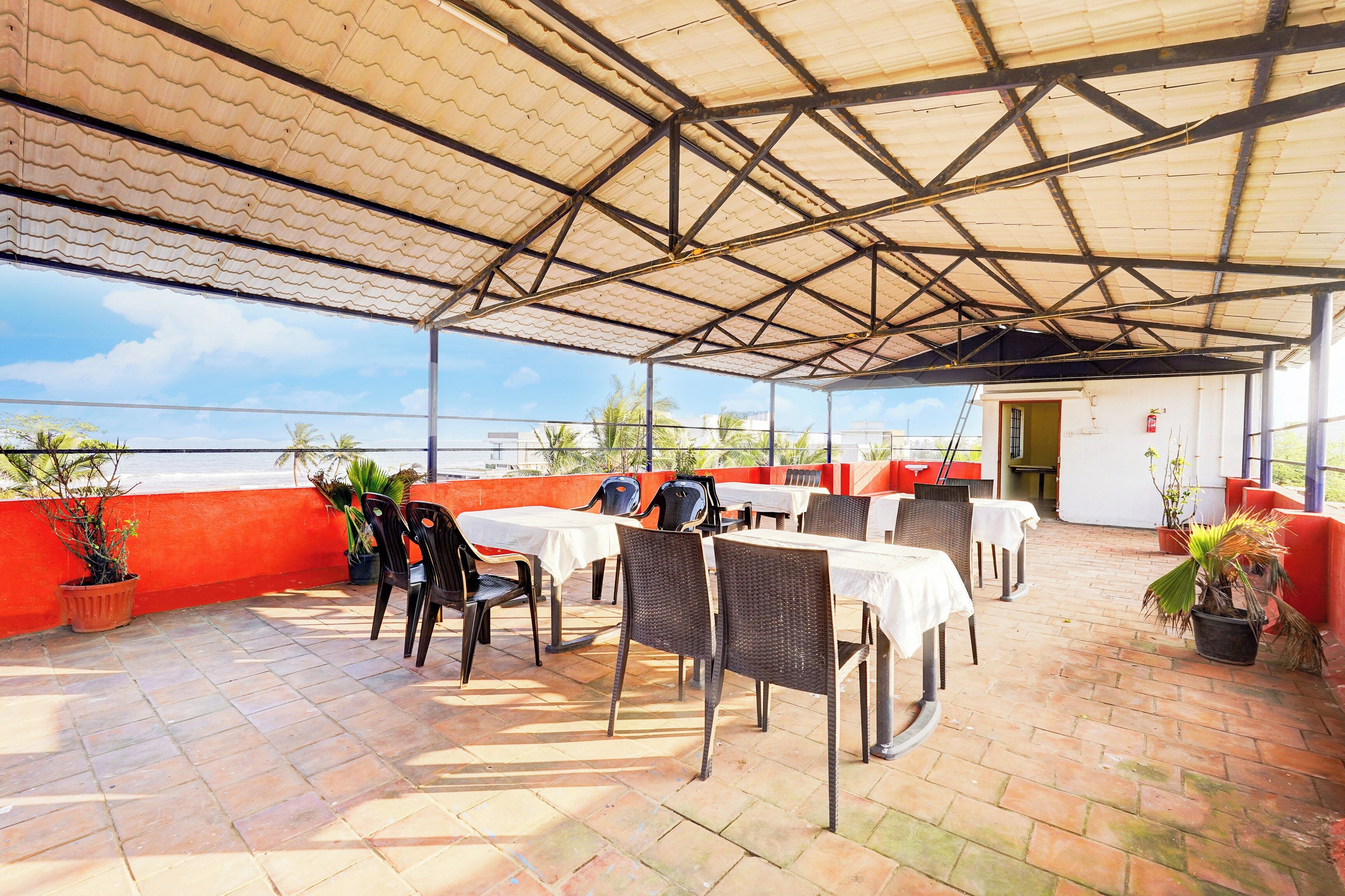 Eine Terrasse im Freien mit Tischen und Stühlen, einer roten Wand und Blumentöpfen.