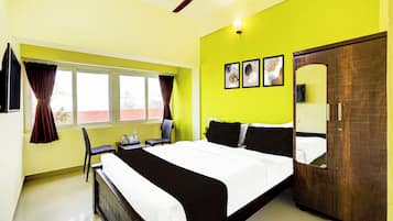 Ein Hotelzimmer mit Bett, Schreibtisch, Stuhl, einem Fenster mit Vorhängen, einem Deckenventilator und Bildern an der Wand.