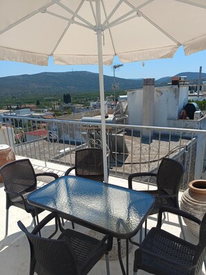 A rooftop terrace with a table and chairs, a white umbrella, and a view of a mountainous landscape. - Stone House 'Medieval-Style 1905 Stone House' (Πυργί)