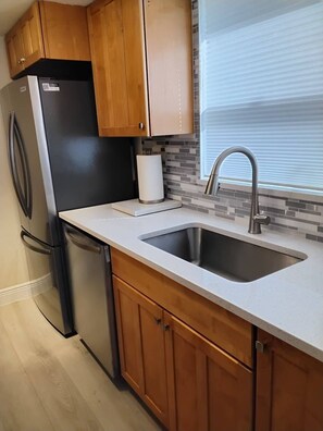 A kitchen with wooden cabinets, a stainless steel sink, and a black refrigerator. - Gulf View Condo w/ 2 Kings | Steps to Beach + Pool (Fort Myers Beach)