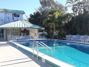 A swimming pool with a covered area, lounge chairs, and a building with a sign. - Gulf View Condo w/ 2 Kings | Steps to Beach + Pool (Fort Myers Beach)