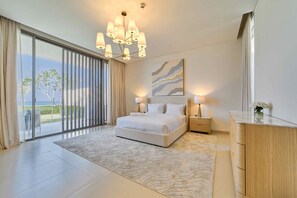 A modern bedroom with a large bed, a chandelier, a painting, and a view of the outdoors. - Sleek 4BR Villa Private Pool Beach Al Zorah (Ajman)