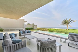 A modern outdoor seating area with a pool, overlooking a beach and ocean. - Sleek 4BR Villa Private Pool Beach Al Zorah (Ajman)