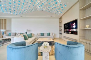A modern living room with a flat-screen TV mounted on the wall, a sofa set, a coffee table, and a decorative ceiling light fixture. - Sleek 4BR Villa Private Pool Beach Al Zorah (Ajman)