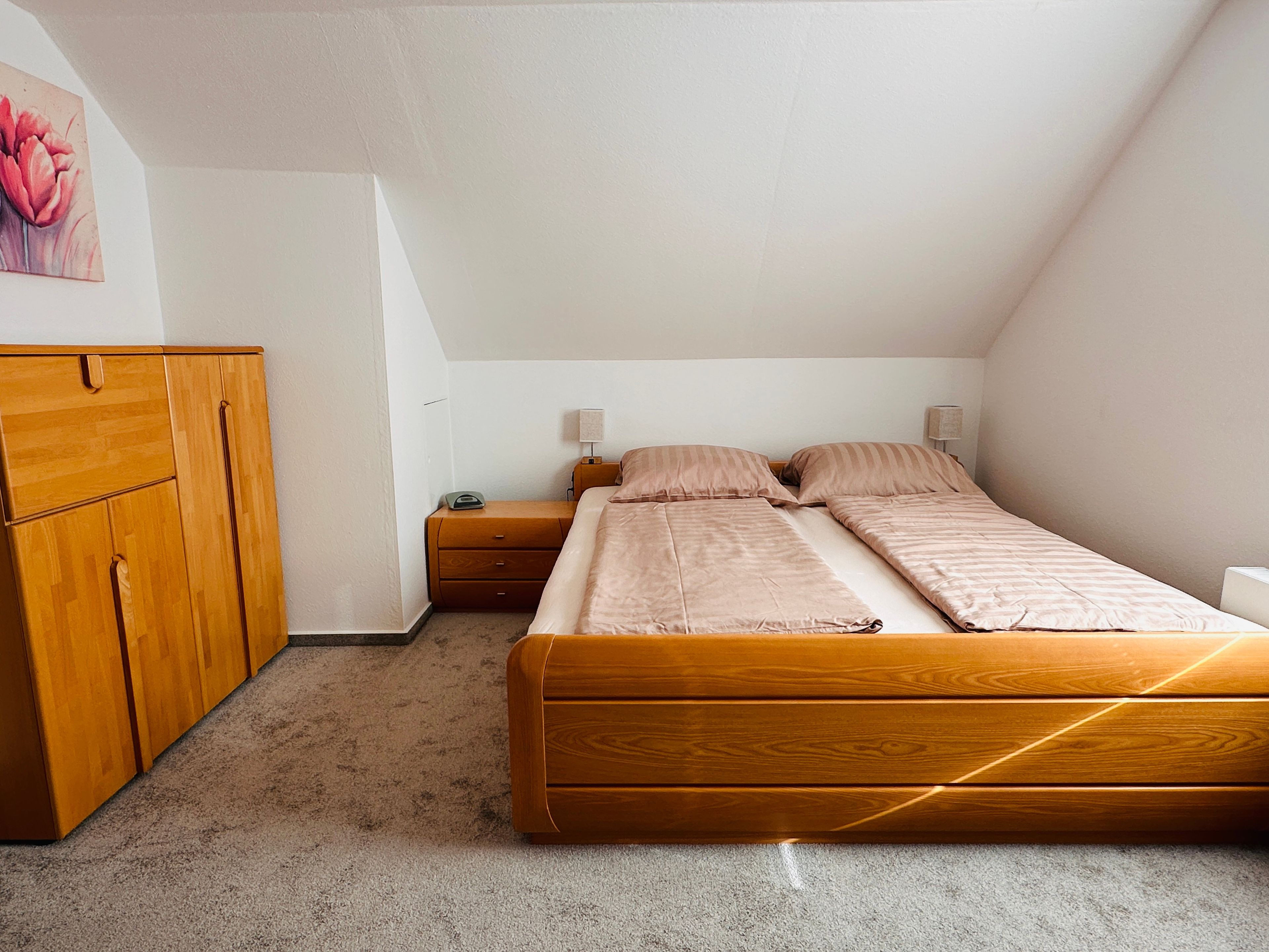 Een slaapkamer met een houten bed, een nachtkastje, een kledingkast en een schilderij aan de muur.