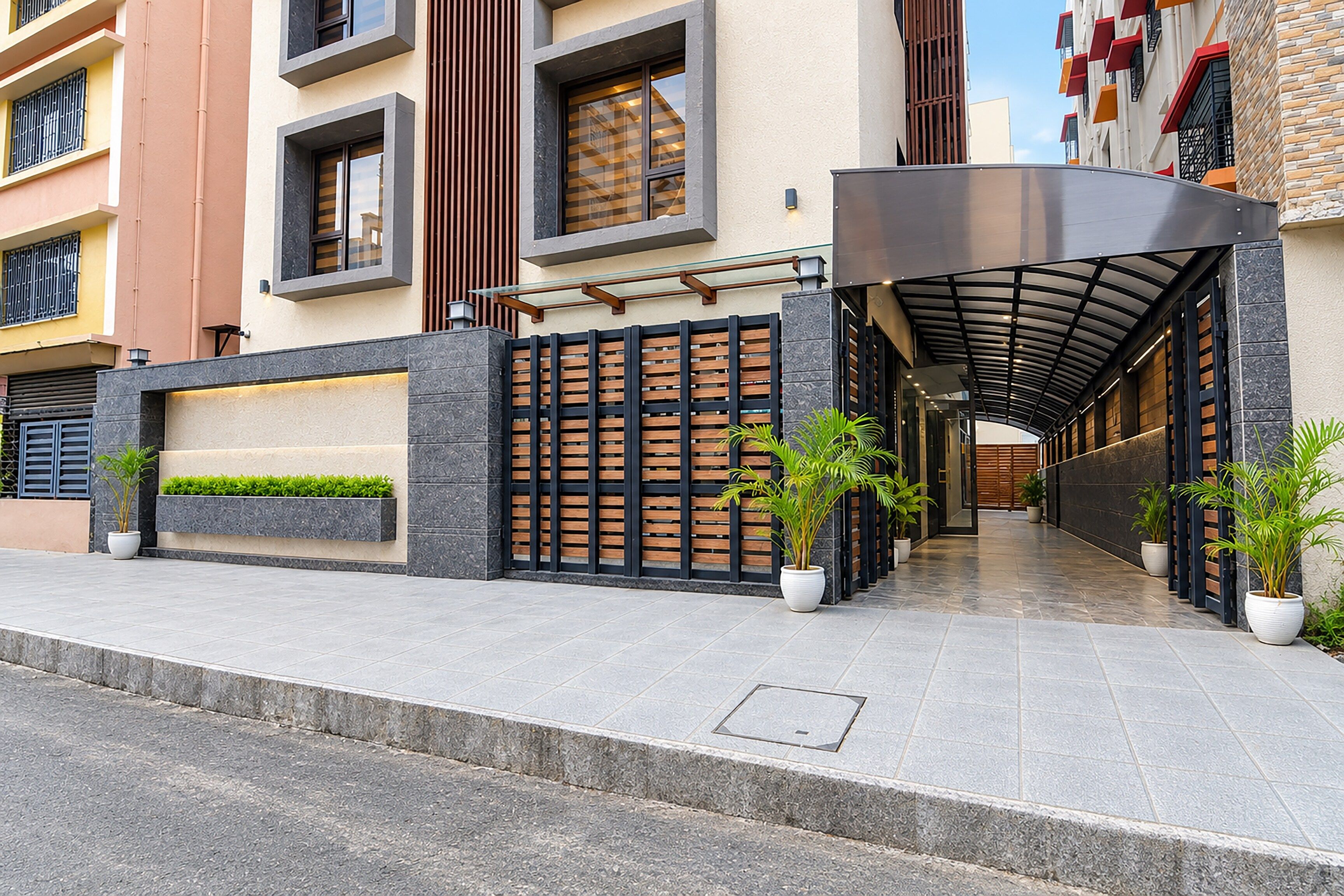 Una entrada moderna a un edificio con un corredor techado, un área con portones y plantas en macetas.